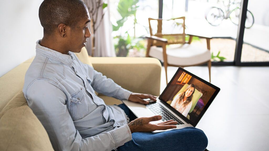 Man sitting on couch, doing teletherapy on his laptop