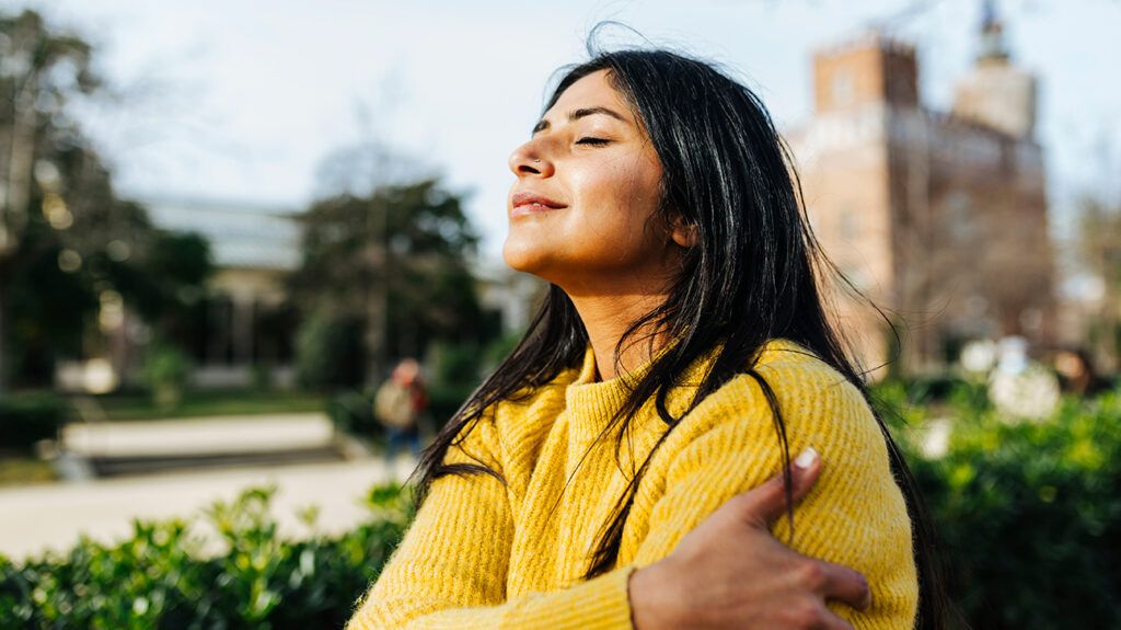 Smiling woman, hugging herself, sitting on a bench outdoors in a park